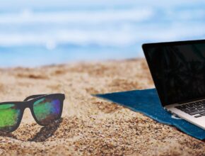 Eine Sonnenbrille und ein Laptop am Strand.