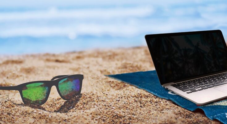 Eine Sonnenbrille und ein Laptop am Strand.