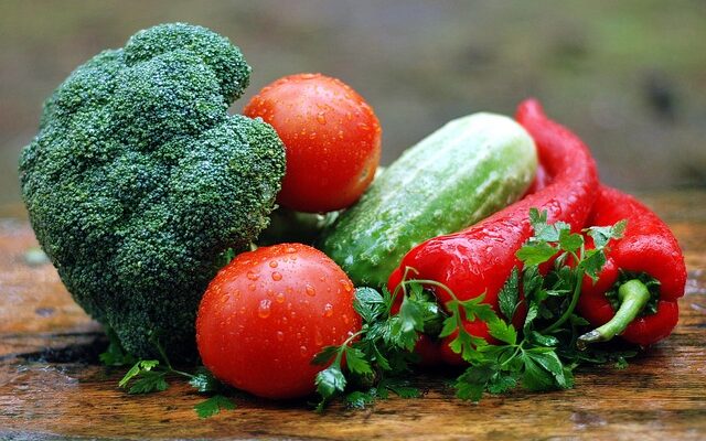 Gemüse: Ein Brokkoli, Tomaten, eine Gurke, rote Paprika und etwas Petersilie auf einem Holzbrett.