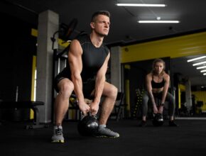 Ein Mann und eine Frau in Kniebeuge in einem Fitnessstudio.