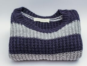 Ein zusammengelegter Strickpulover mit grau-blauen Streifen.