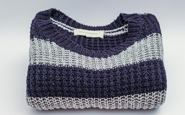 Ein zusammengelegter Strickpulover mit grau-blauen Streifen.