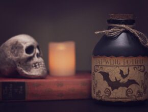 Halloweendeko: Ein Schädel, eine Kerze und daneben eine Flasche mit Gift