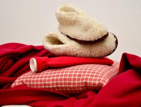 Wärmende Hausmittel: Dicke Pantoffeln, eine Wärmflasche, ein Kissen und eine Decke