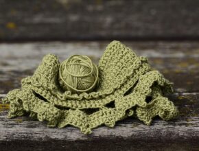 Ein Knäuel grüner Wolle, darunter ein Stück Gestricktes.