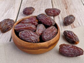 Ein paar Datteln, die in einer kleinen Holzschale und daneben liegen.